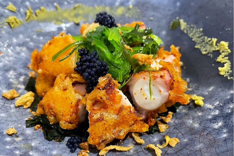 Scallop with caviar, greens and vegetable crisps plated on slate