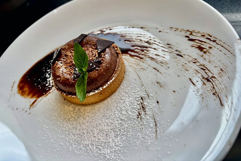 Chocolate soufflé dusted with icing sugar, with chocolate shavings and a basil leaf on a white plate